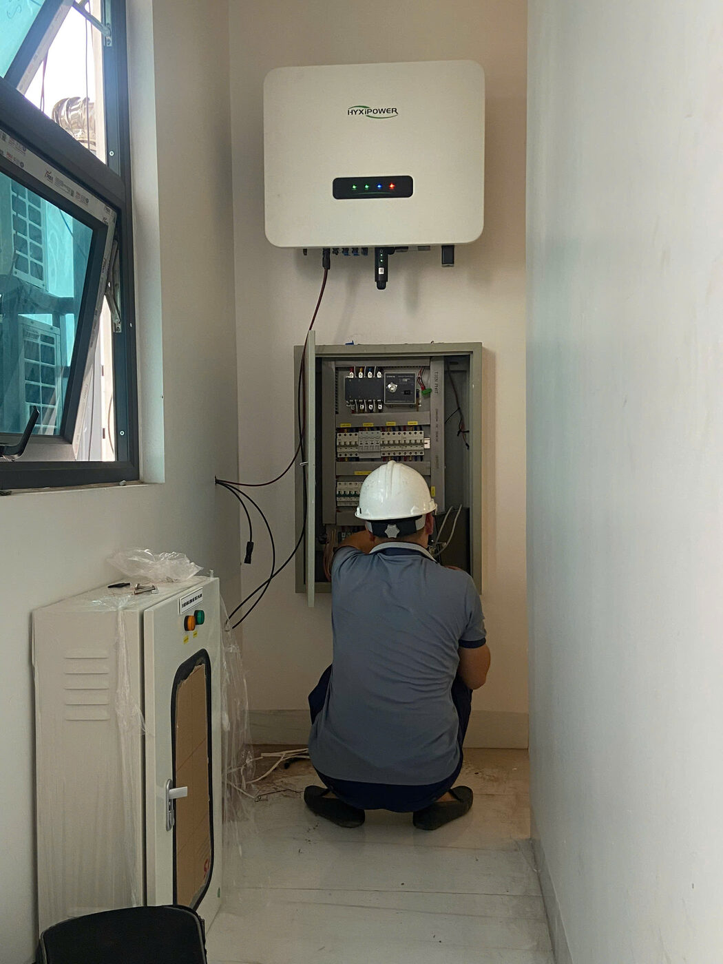 Kỹ thuật viên đội mũ bảo hộ đấu tủ điện cạnh pin lưu trữ